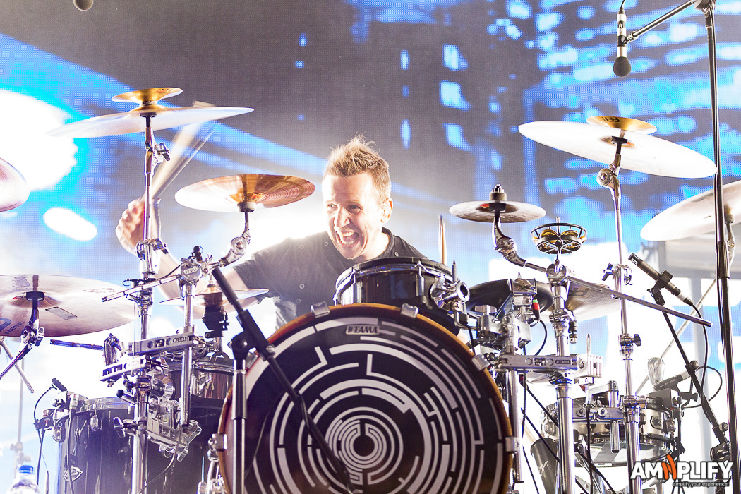 KJ Sawka grinning behind the Tama drum kit performing with Pendulum live with blue stage lighting
